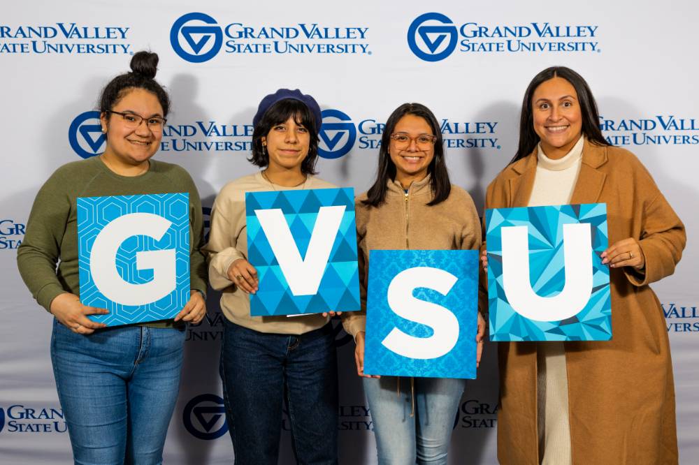 individuals smiling with gvsu sign and tan jacket